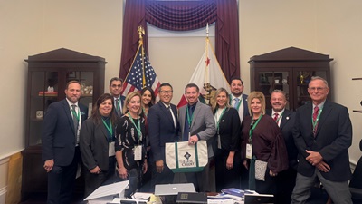 Group of Farm Credit representatives and partners standing together in a government office, with U.S. and California flags behind them, holding a Farm Credit tote bag.